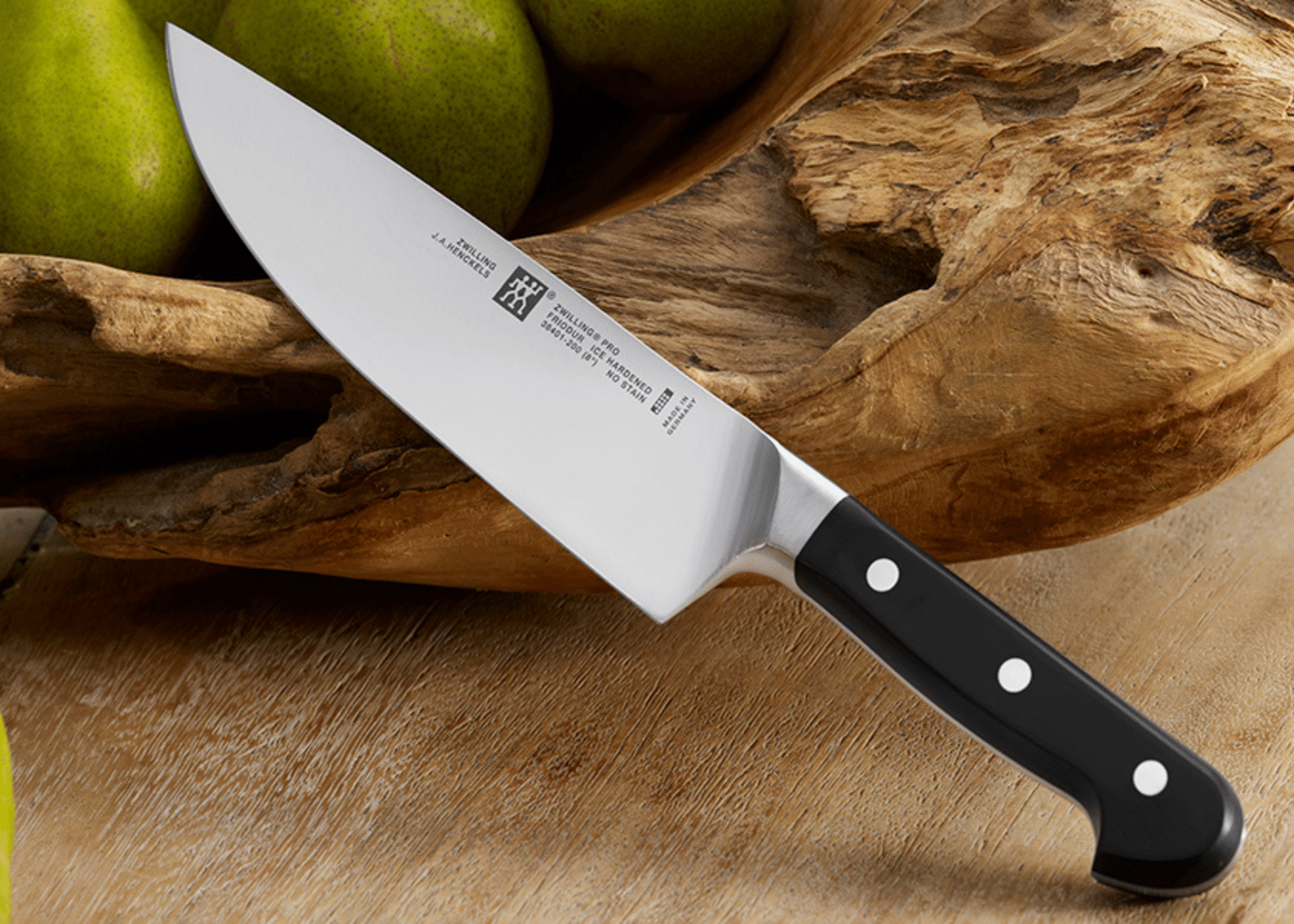 A Chefs knife on a counter with fruit and wood