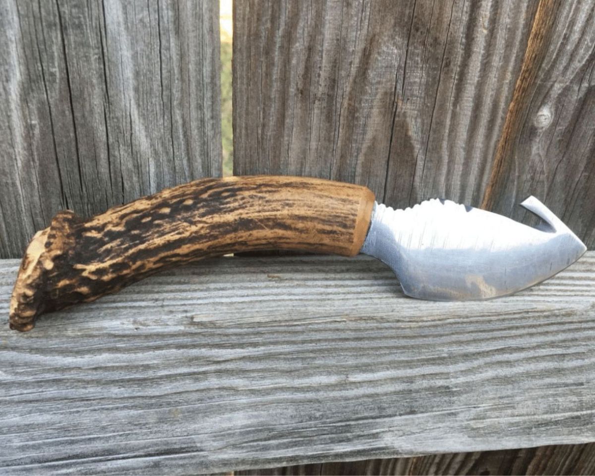 Custom stag handle skinning knife with gut hook on weathered wood fence