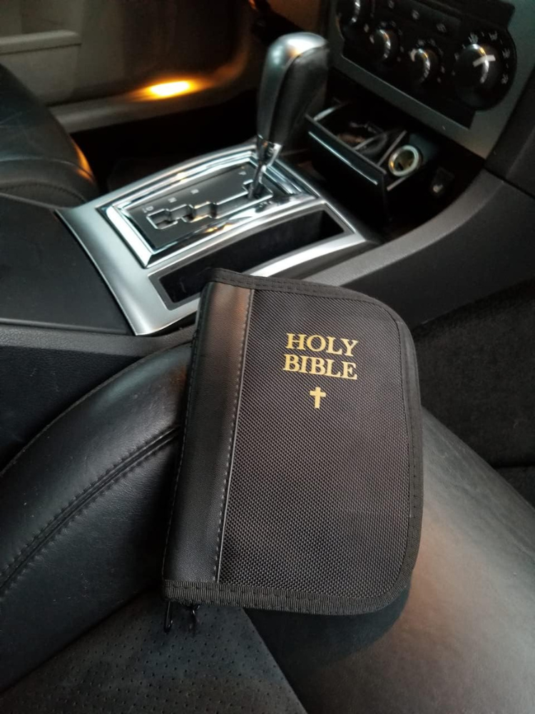 A gun inside a gun safe bible on a black leather car seat.