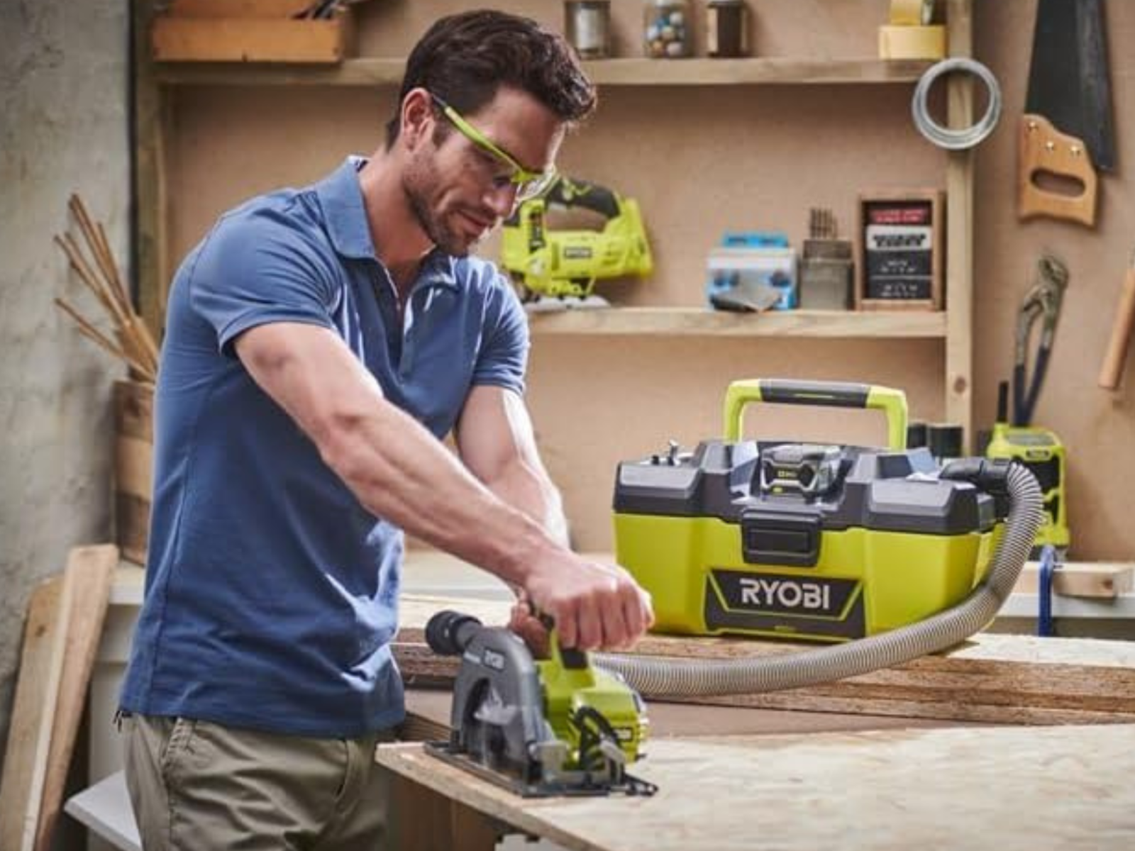 A man using a Ryobi cordless saw with a cordless vacuum as a dust catcher while cutting wood.