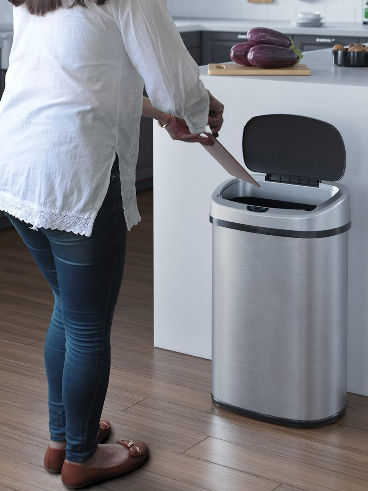 A woman standing in front of an automatic open stainless steel garbage can